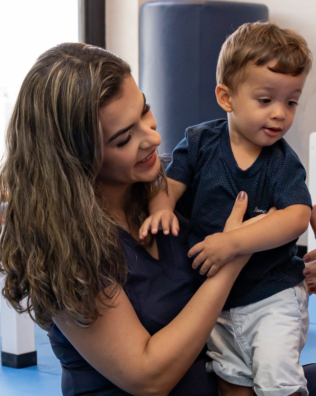 Letícia Dutra sorrindo com uma criança pequena no colo durante uma avaliação